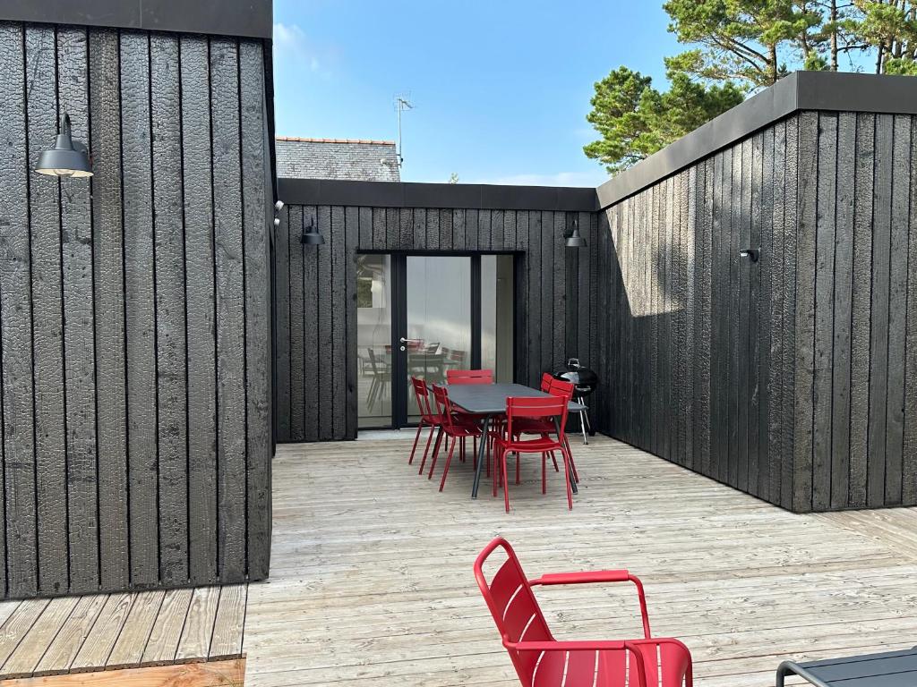un patio avec des chaises rouges et une table sur une terrasse en bois dans l'établissement Ty-Du - Plage du Sillon - Parking Privé - Ile Tudy, à l'Île-Tudy