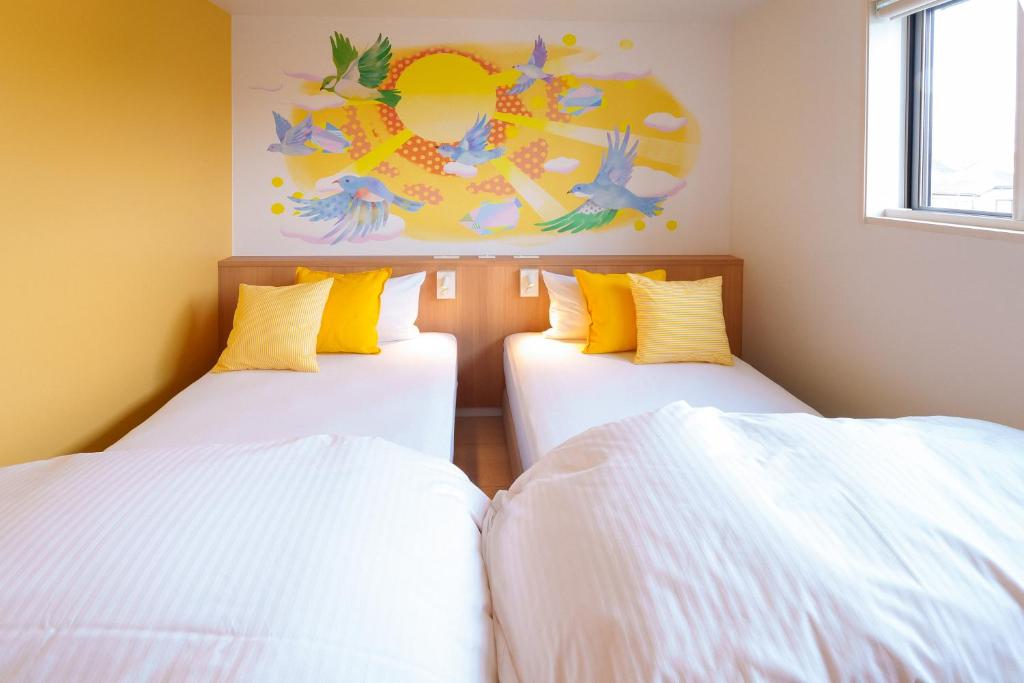 two beds in a room with white sheets and yellow pillows at Stay&resort Luce ルーチェ in Urayasu
