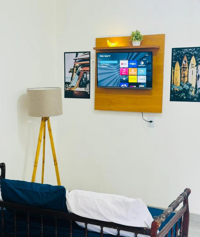 a tv on a wall with a couch in a room at Studio Vista Linda 2 - Acesso a Riviera e Centro Kitnet in Bertioga