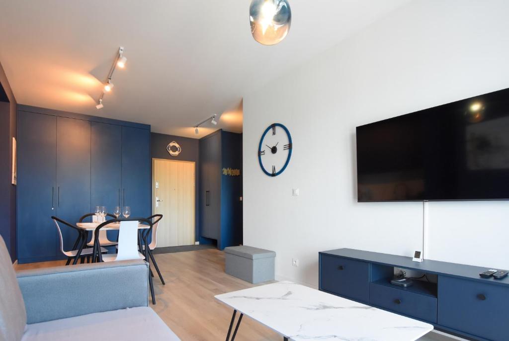Una sala de estar con una mesa y un reloj en la pared. en VacationClub - Let's Sea Baltic Park Apartament F96, en Gąski