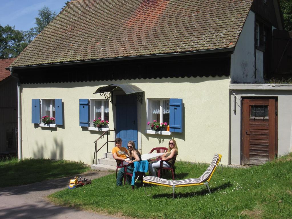 three people sitting in the grass in front of a house at Hofgut Duerrenbuehl in Grafenhausen