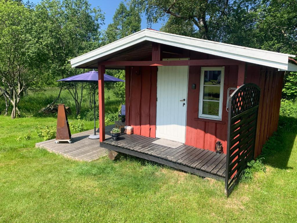 a red and white shed with a wooden deck at Riverside Bliss - Cozy Cabin near Tvedestrand with WiFi and Deck in Vegårshei