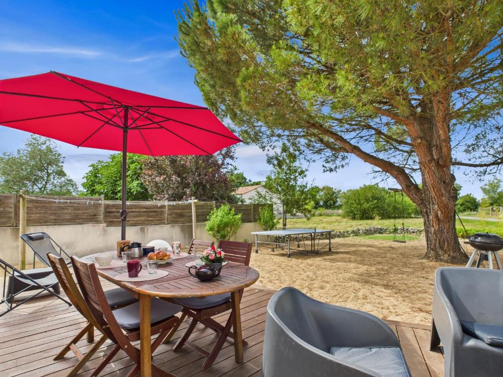 une terrasse en bois avec une table et un parasol rouge dans l'établissement Maison familiale et colorée avec jardin pour 6, à Saligottière