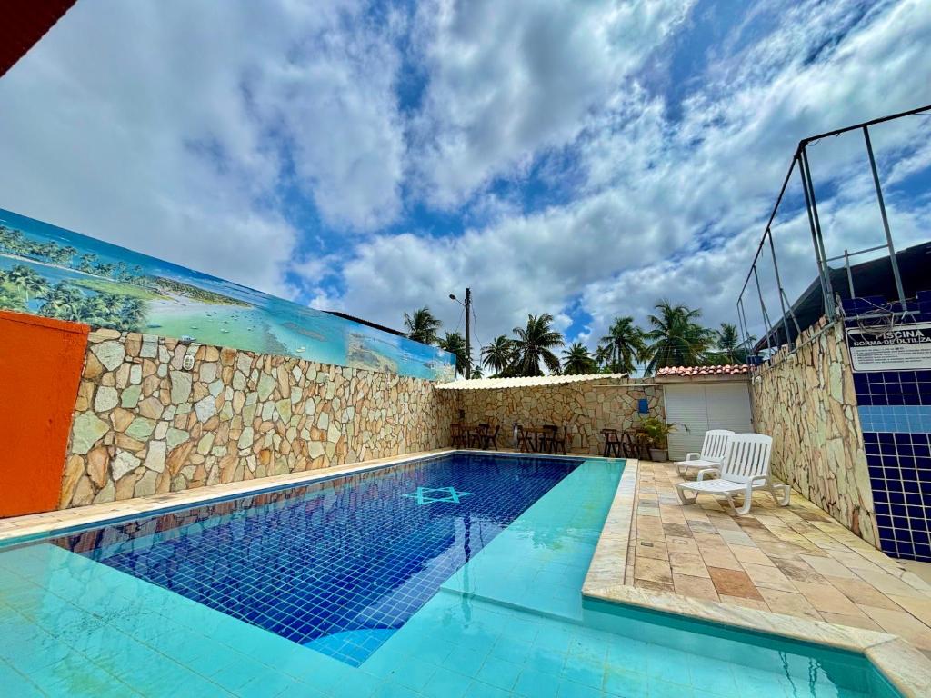 een zwembad naast een stenen muur met een blauwe bij Pousada Meu Xodó in São Miguel dos Milagres