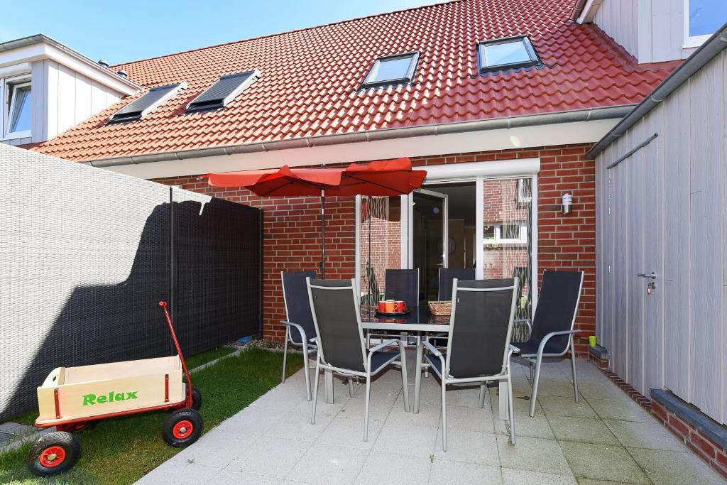 a patio with a table with chairs and an umbrella at Ferienhaus Relax - Uns Huus an t Küst in Bensersiel