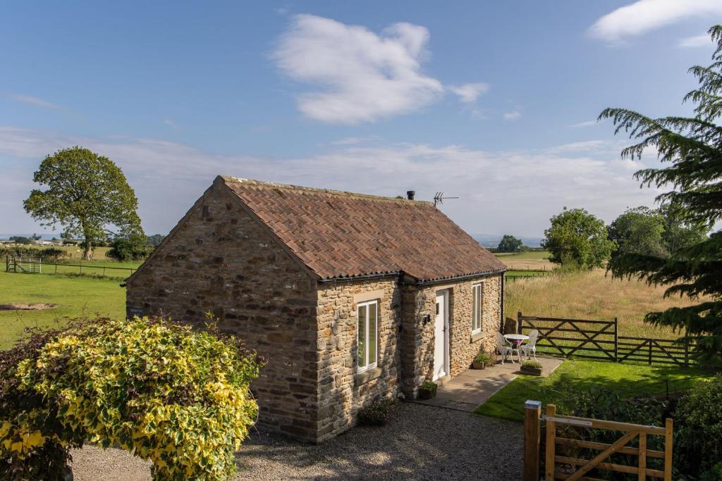 a small brick building in a field with a fence at Honey Pot Barn in Cropton