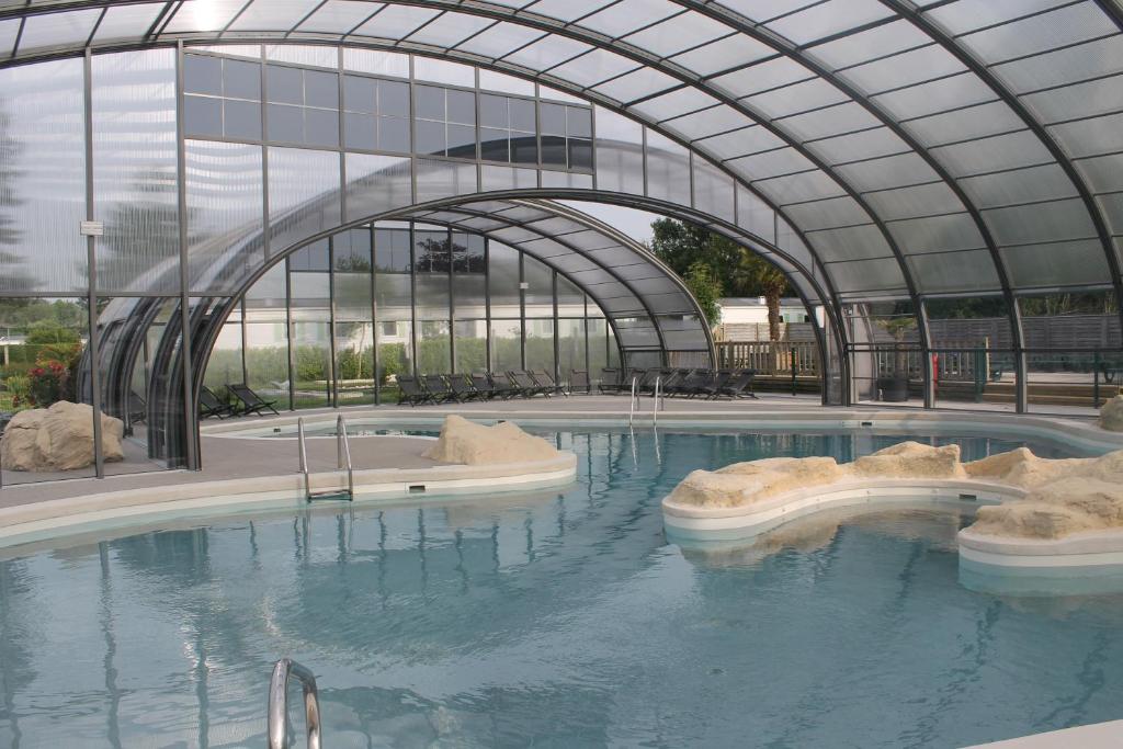 a swimming pool in a building with an open roof at Camping des Roses in Quend