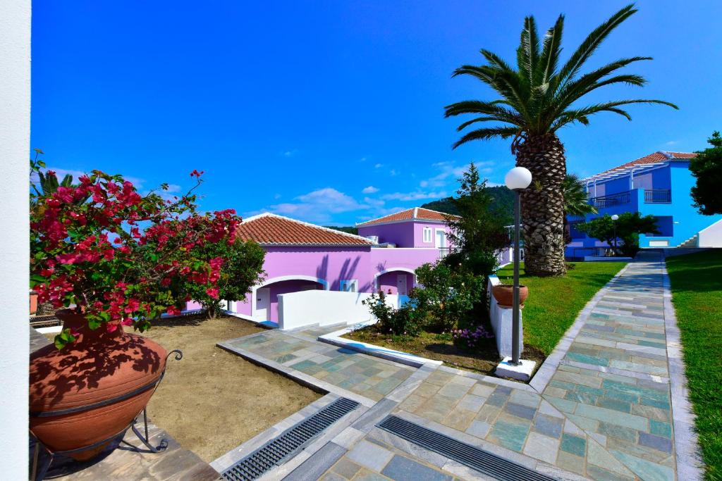 a courtyard with a palm tree and a pink house at Arion Hotel in Kokkari