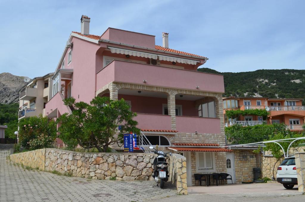a pink house on top of a stone wall at Apartments & Rooms Nensi in Baška