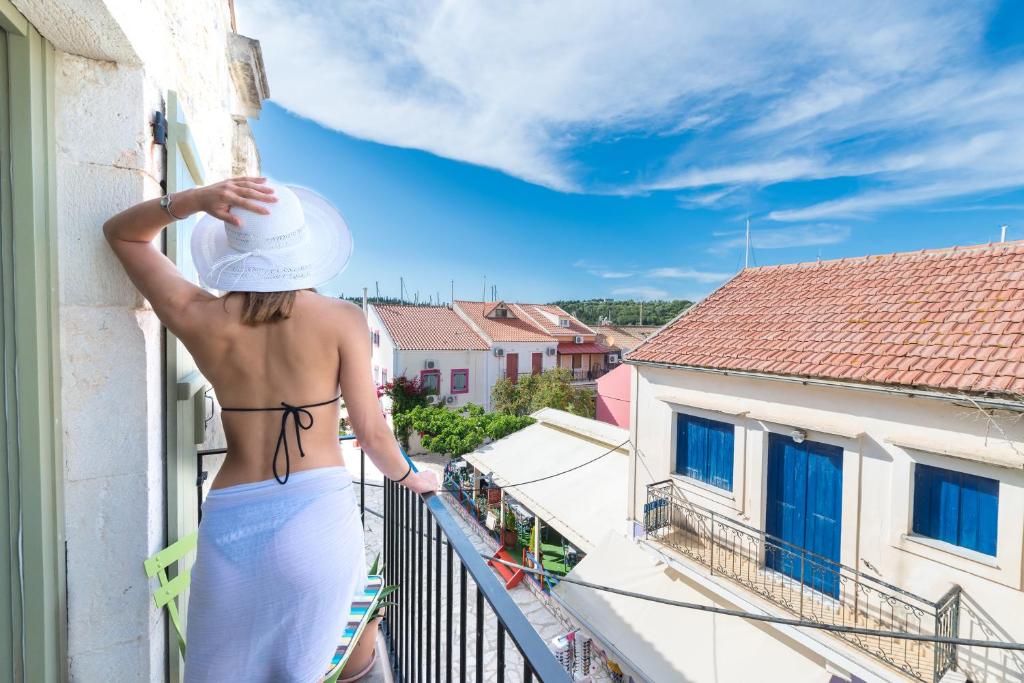 una mujer con un vestido blanco y un sombrero en un balcón en Fiscardonna Luxury Suites, en Fiskardho