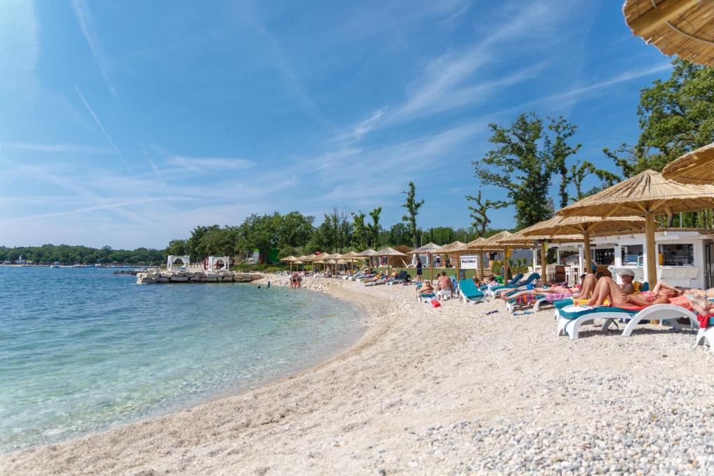 a beach with chairs and umbrellas and people on it at Dubravka 1 in Funtana