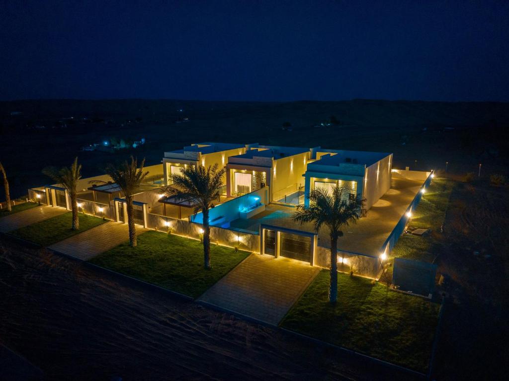 a building with a pool and palm trees at night at Remal Resort Bidiyah in Badīyah