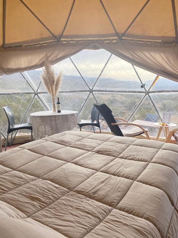 a large bed in a tent with a table and chairs at Terrana Ecolodge Mountain Domes in Ciudad Lujan de Cuyo