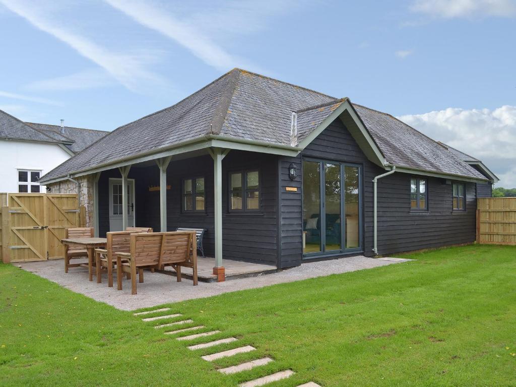 a black house with a table and benches in a yard at Robin Cottage - Ukc3436 in Newton Abbot