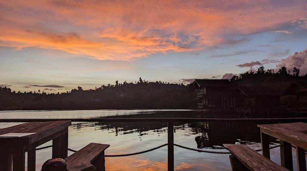 un tramonto su uno specchio d'acqua con panchine di legno di Logbond Cozy Guesthouse a Pulau Saonek-kecil