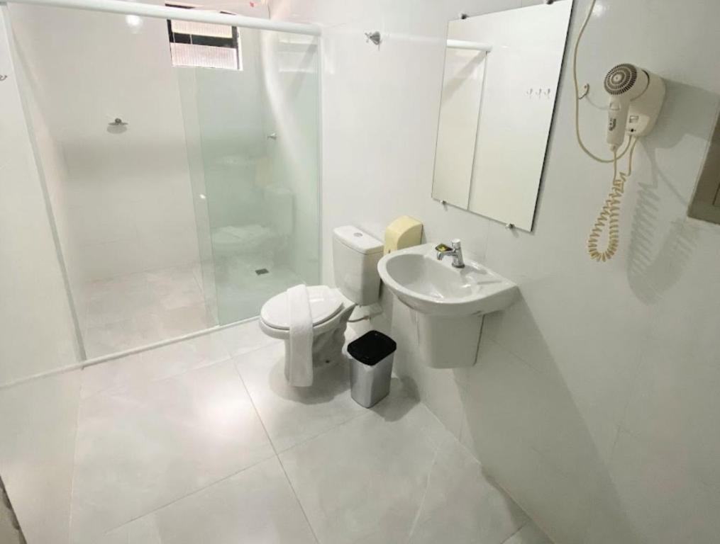 a white bathroom with a toilet and a sink at Itaipu Hotel in Foz do Iguaçu