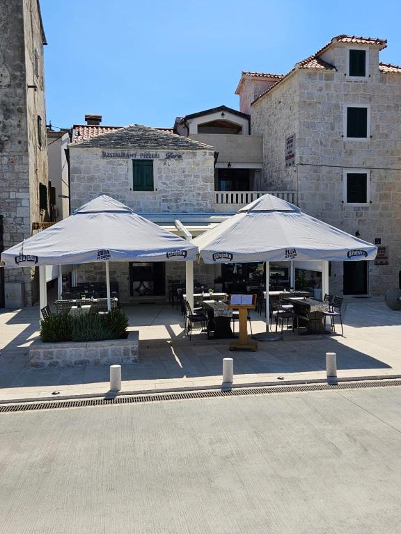 two white umbrellas with tables and chairs in front of a building at Guest house Jere Old Town in Rogoznica