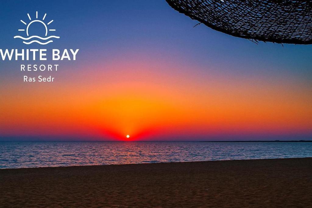 a sunset on the beach with the words white bay resort reset at White Bay Ras Sedr وايت باي راس سدر in Ras Sedr