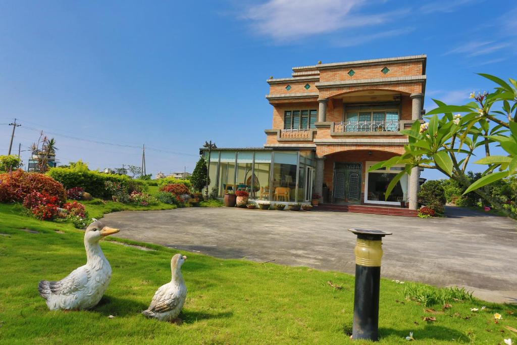 two geese standing in the grass in front of a house at Campestral Garden in Jiaoxi