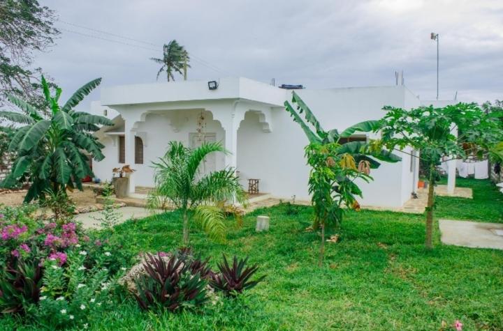 a white house with trees and plants in front of it at Red Land House in Watamu