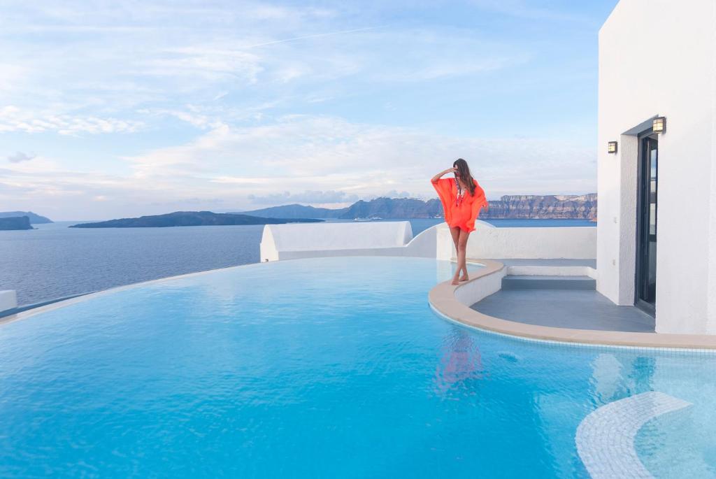 a woman in an orange dress standing on the edge of a swimming pool at Ambassador Aegean Luxury Hotel & Suites in Akrotiri