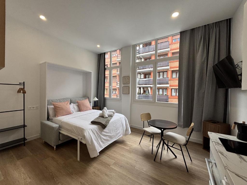 a bedroom with a bed and a table and two windows at Gabika Apartment 1 in Bilbao
