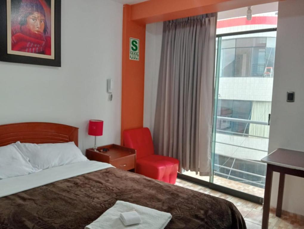 a bedroom with a bed and a red chair and a window at Gran Hotel Leguia in Cajamarca