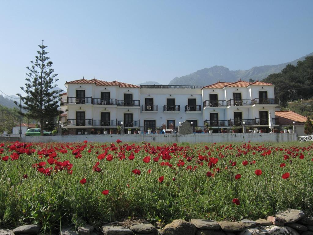 un grand bâtiment blanc avec un champ de fleurs rouges dans l'établissement Hotel Apartment Agios Konstantinos, à Ágios Konstantínos