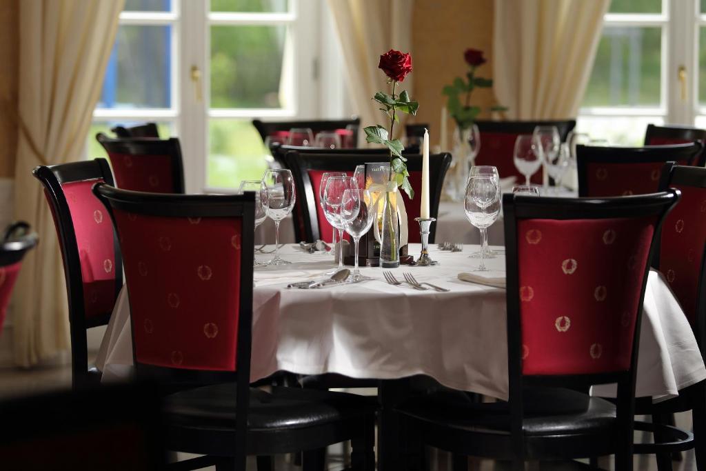 Elegantly set restaurant table with red chairs, wine glasses, single rose and candle.