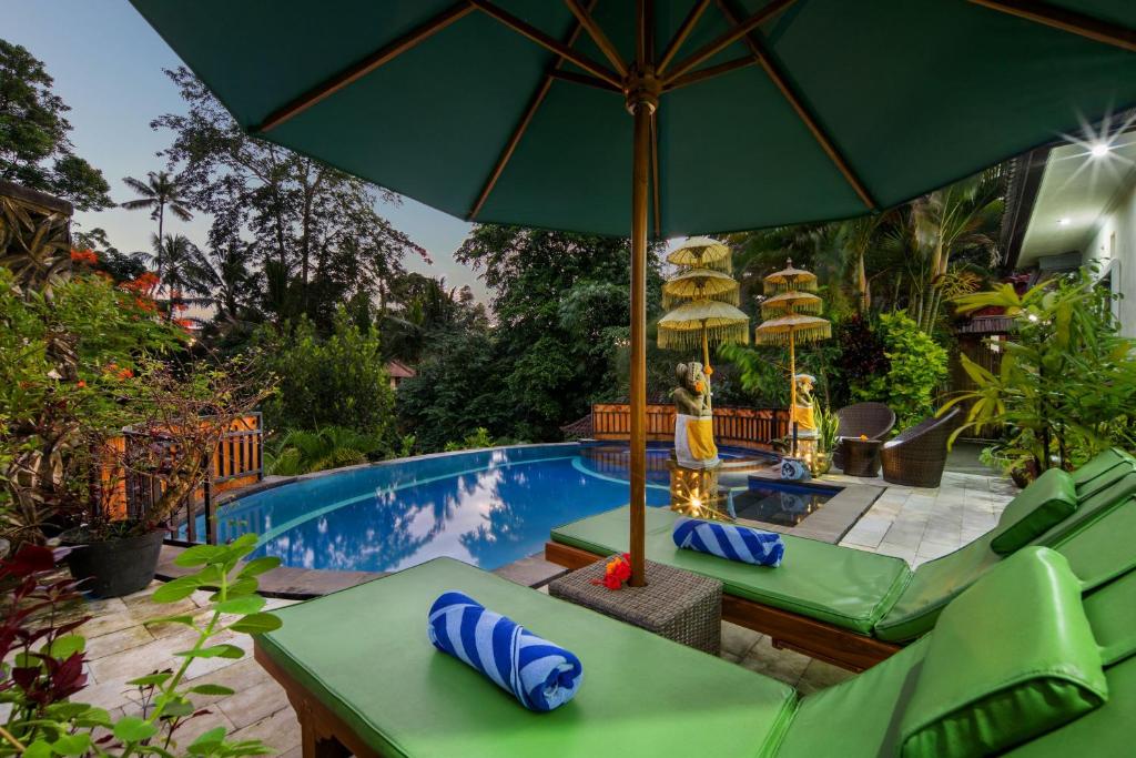 a swimming pool with green chairs and an umbrella at Villa Bakti Ubud by kamara in Ubud