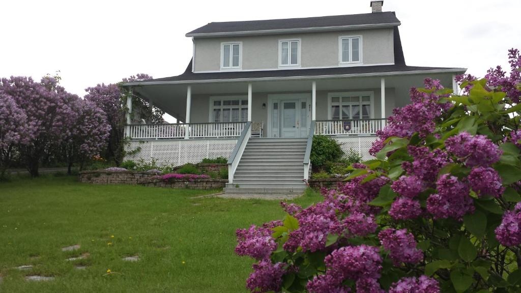 a white house with purple flowers in the yard at Maison des lilas in La Malbaie