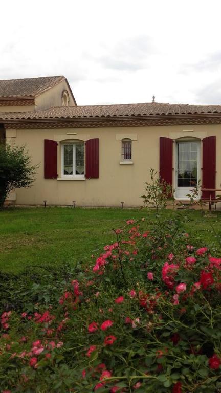 a house with red shutters and flowers in the yard at Maison d'Hôtes Afrika du Queyroux in Ginestet