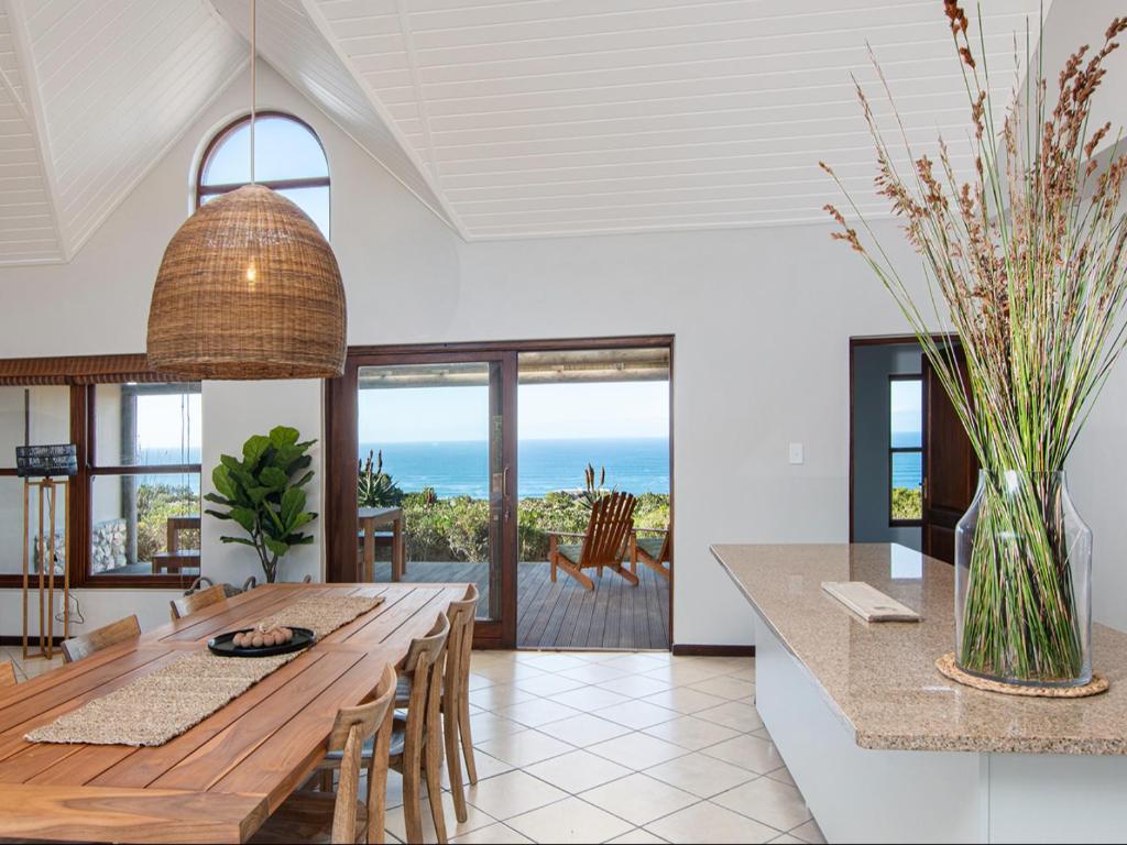 a dining room with a table and a view of the ocean at Elysian Bay Cottage in Boggomsbaai