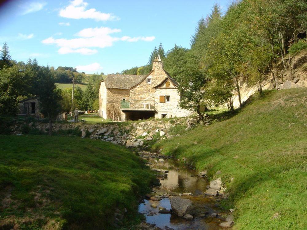 Una antigua casa de piedra en una colina junto a un arroyo. en Le Moulin de Graunès, en Moyrazès