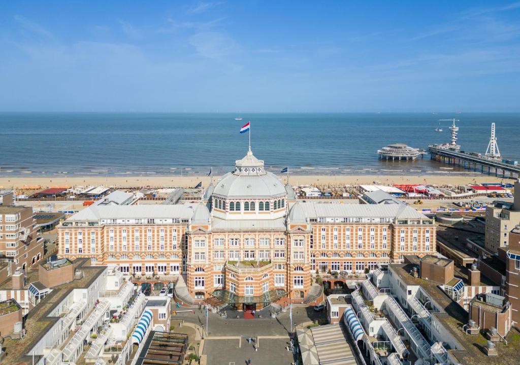 a building with a flag on top of it next to the ocean at Grand Hotel Amrâth Kurhaus The Hague Scheveningen in Scheveningen