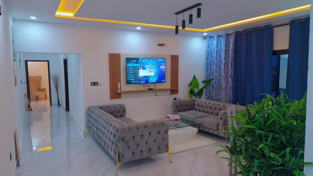 een woonkamer met banken en een tv aan de muur bij Aloha Suites Odza - by Skyline Residence Services in Yaoundé