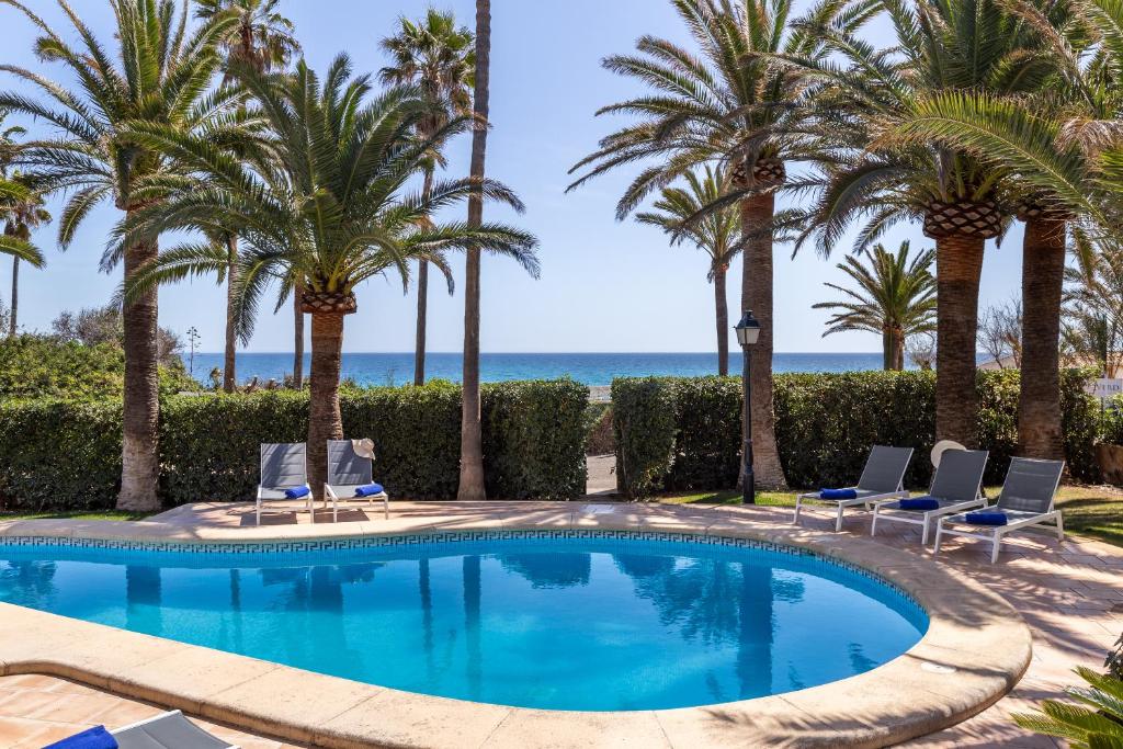 Una piscina con palmeras y sillas y el océano. en Sembat de Mar, en Cala Millor