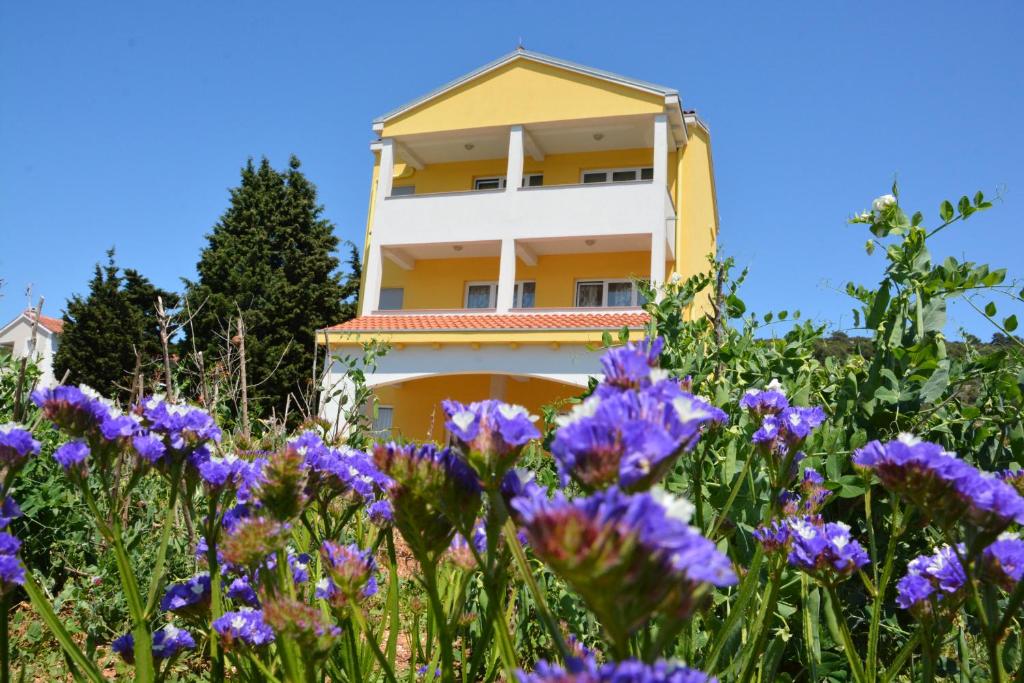 ein gelbes und weißes Gebäude mit lila Blumen im Vordergrund in der Unterkunft Apartments Buturi in Soline