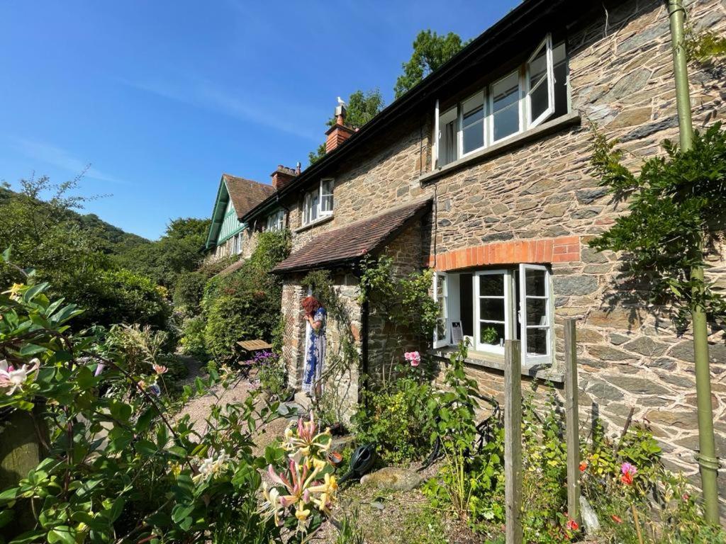 an old stone house with flowers in front of it at Sheila's Cottage in Lynton