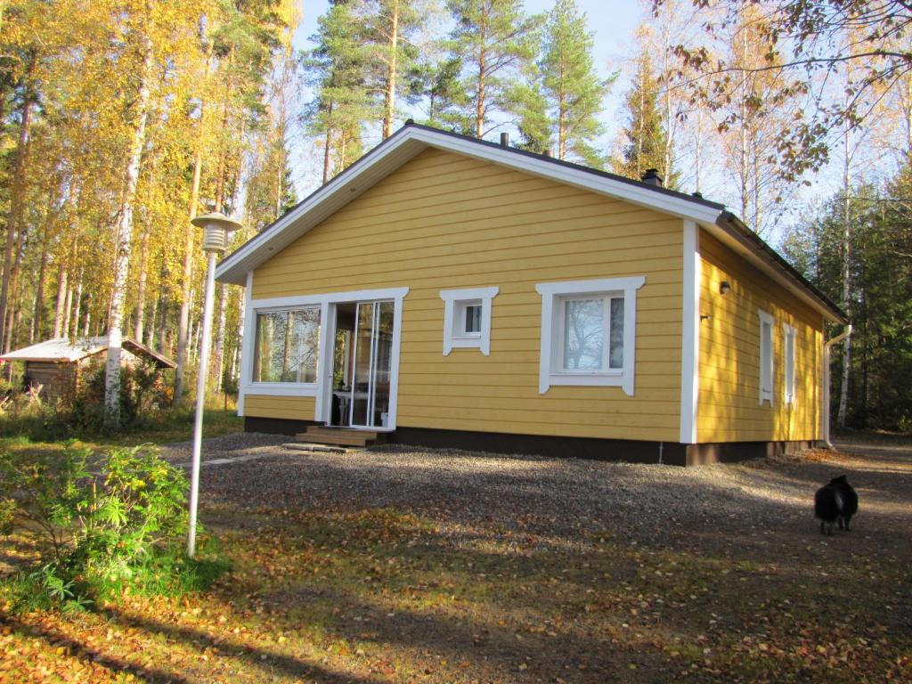 une maison jaune avec un chat debout devant elle dans l'établissement Kaijonselän mökit Pyhitty, à Vehmaskylä