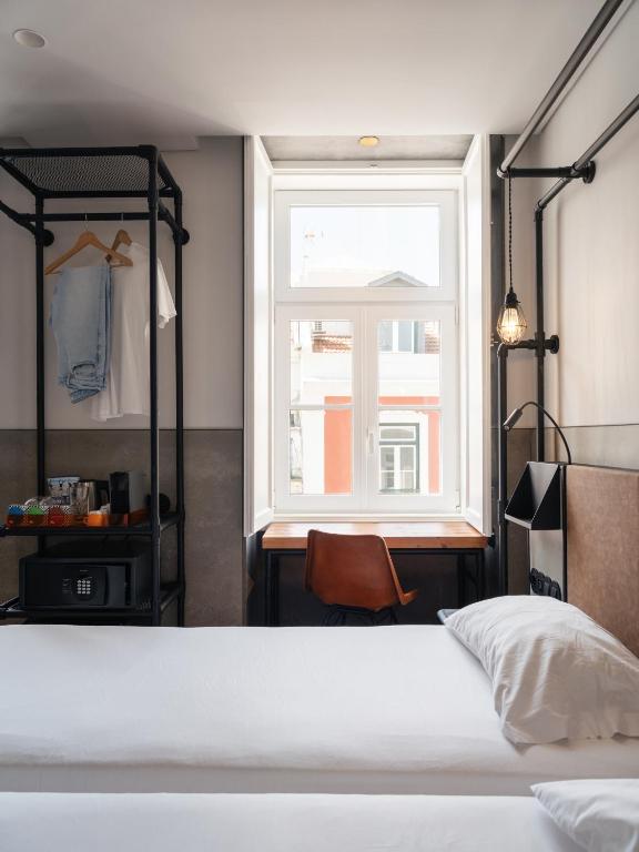 A compact double bedroom with a window-side desk and open hanging storage.