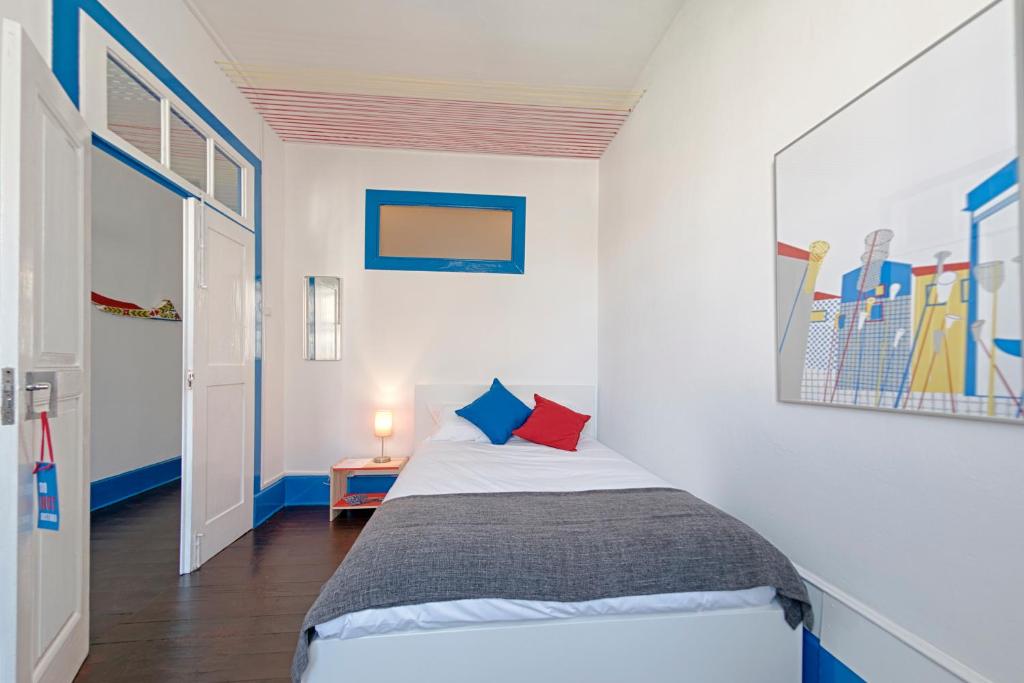 um pequeno quarto com uma cama com almofadas azuis e vermelhas em Ponto de Abrigo em Aveiro