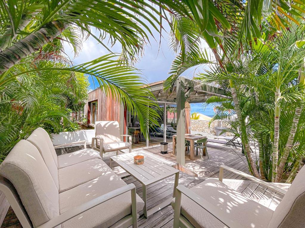 a patio with white chairs and a table and palm trees at Le Lodge SXM luxe in Cul de Sac