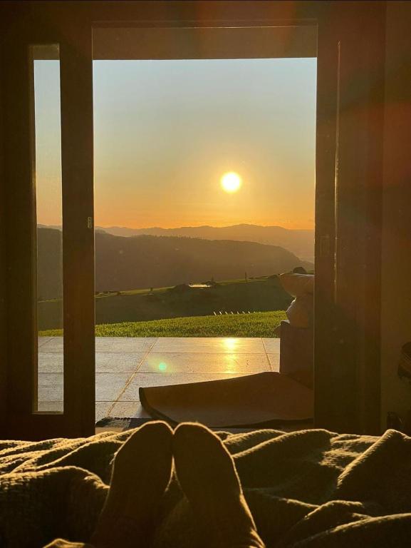 a person laying on a bed looking out a window at the sunset at VisttaSC in Praia Grande