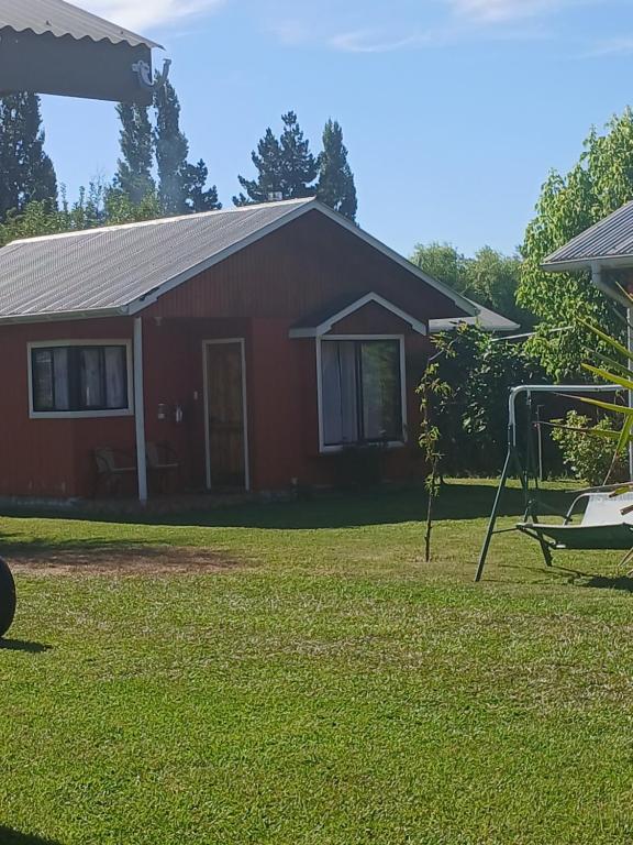 a red house with a yard with a swing at Cabañas La Palmera saltos del Laja in Los Ángeles