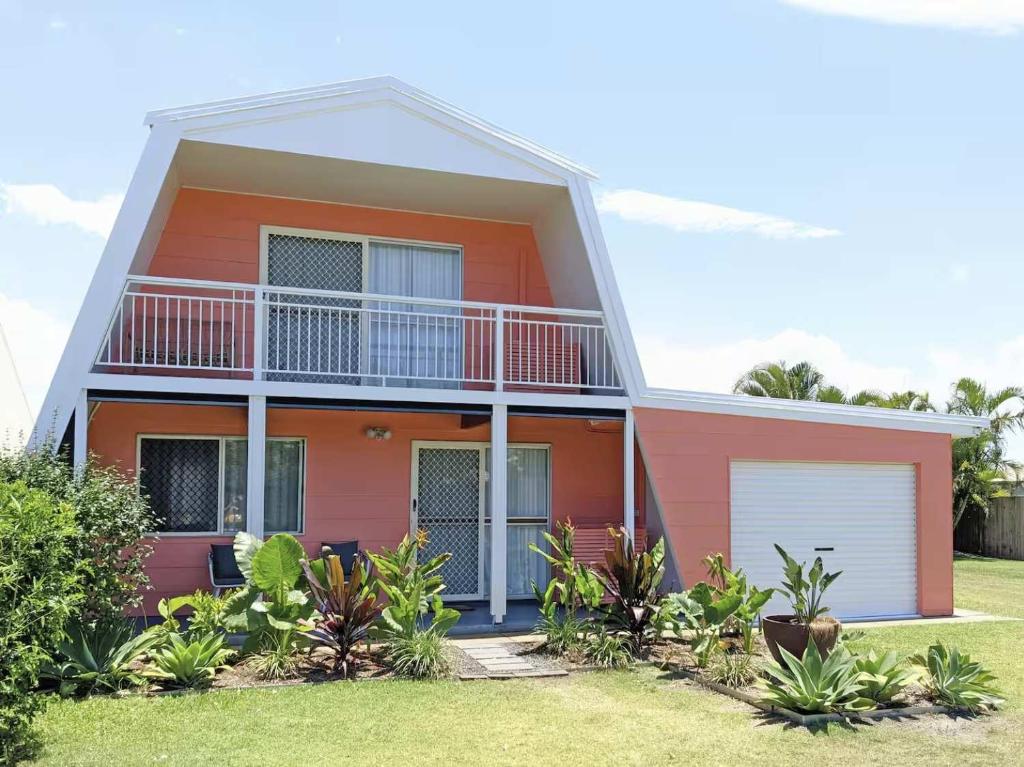 a red house with a balcony on top of it at Central Bargara Beach Bungalow by UG in Bargara