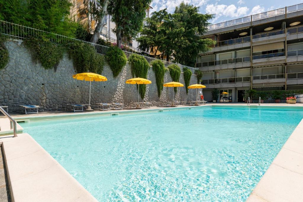 ein Swimmingpool mit gelben Sonnenschirmen und einem Gebäude in der Unterkunft GuestHost - Modern Escape with Pool & Sunny Terrace in Sanremo