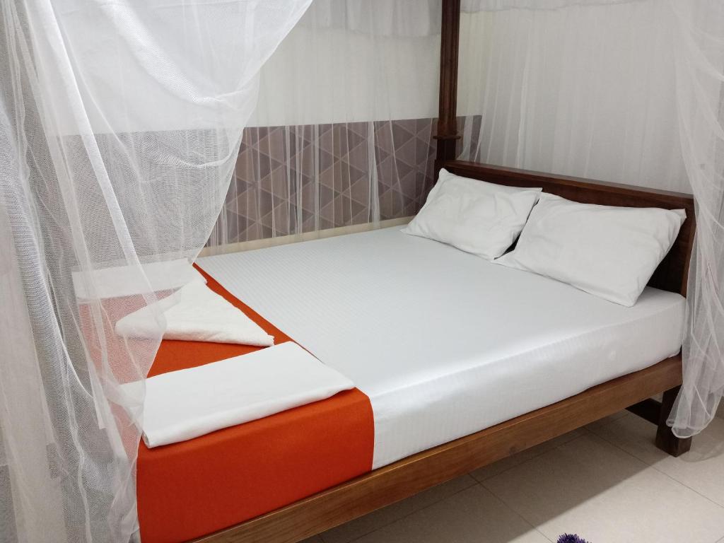 a bed with white sheets and orange and white pillows at New Toropi Homestay in Gadaladeniya