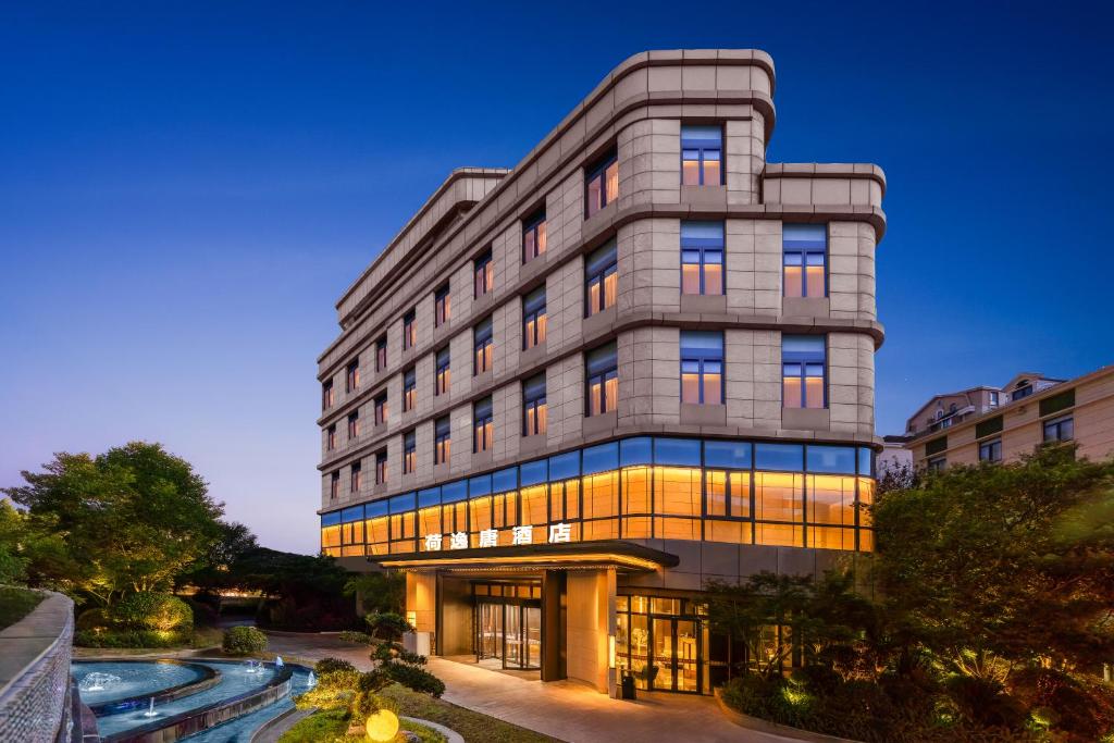上海上海虹桥荷逸唐酒店北新泾地铁站Shanghai Hongqiao Heyitang Hotel Beixinjing Subway Station Branch的一座灰色的高楼，前面有一个池塘