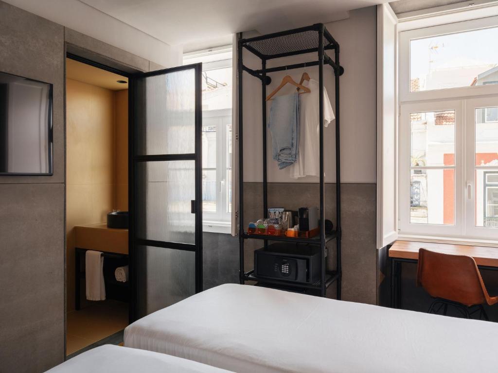 A compact guest room with a double bed, open clothing rack, desk and street-facing window.